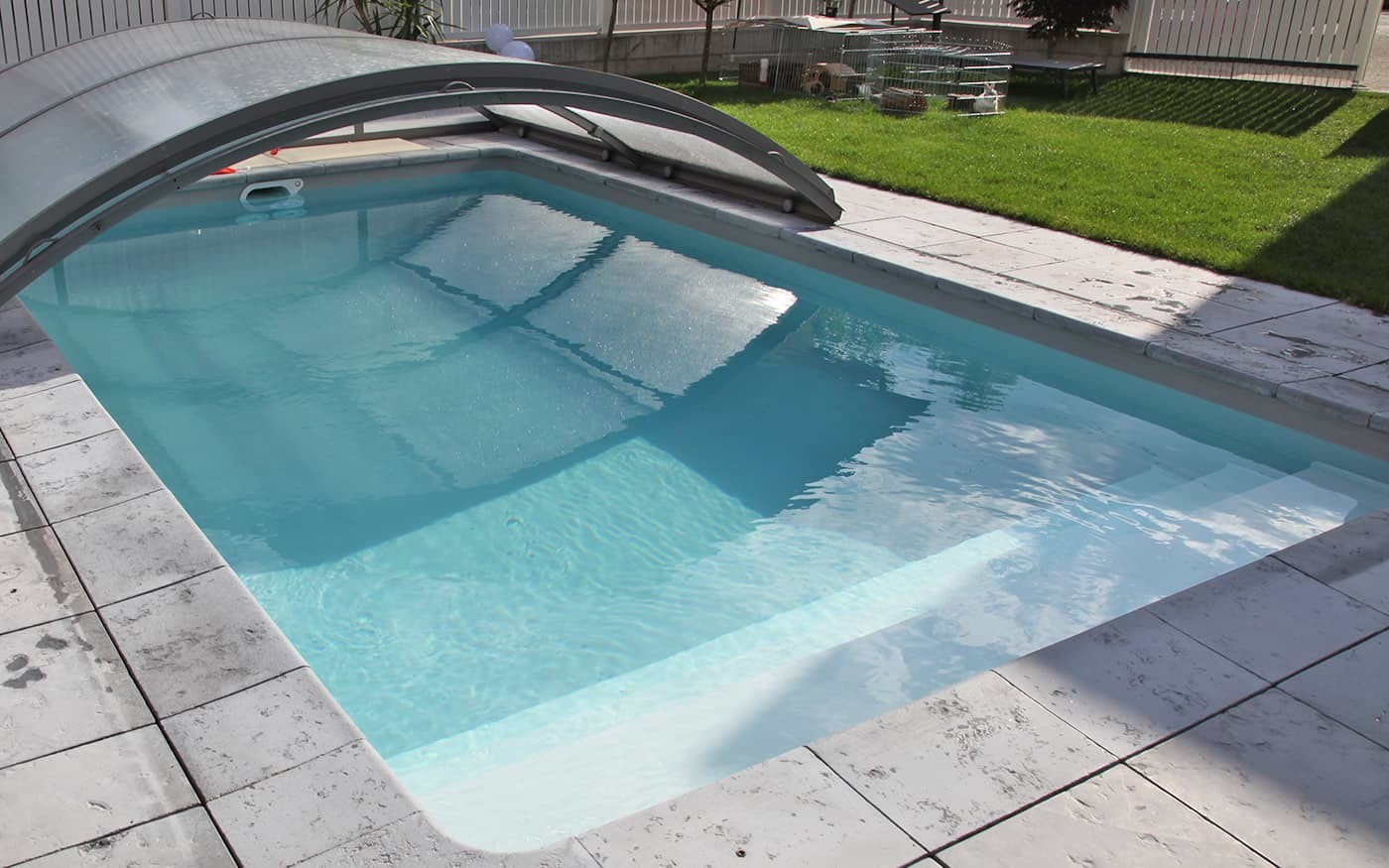 &Uuml;berdachter Swimmingpool Desjoyaux mit klarem Wasser, umgeben von gefliesten Boden und Rasen