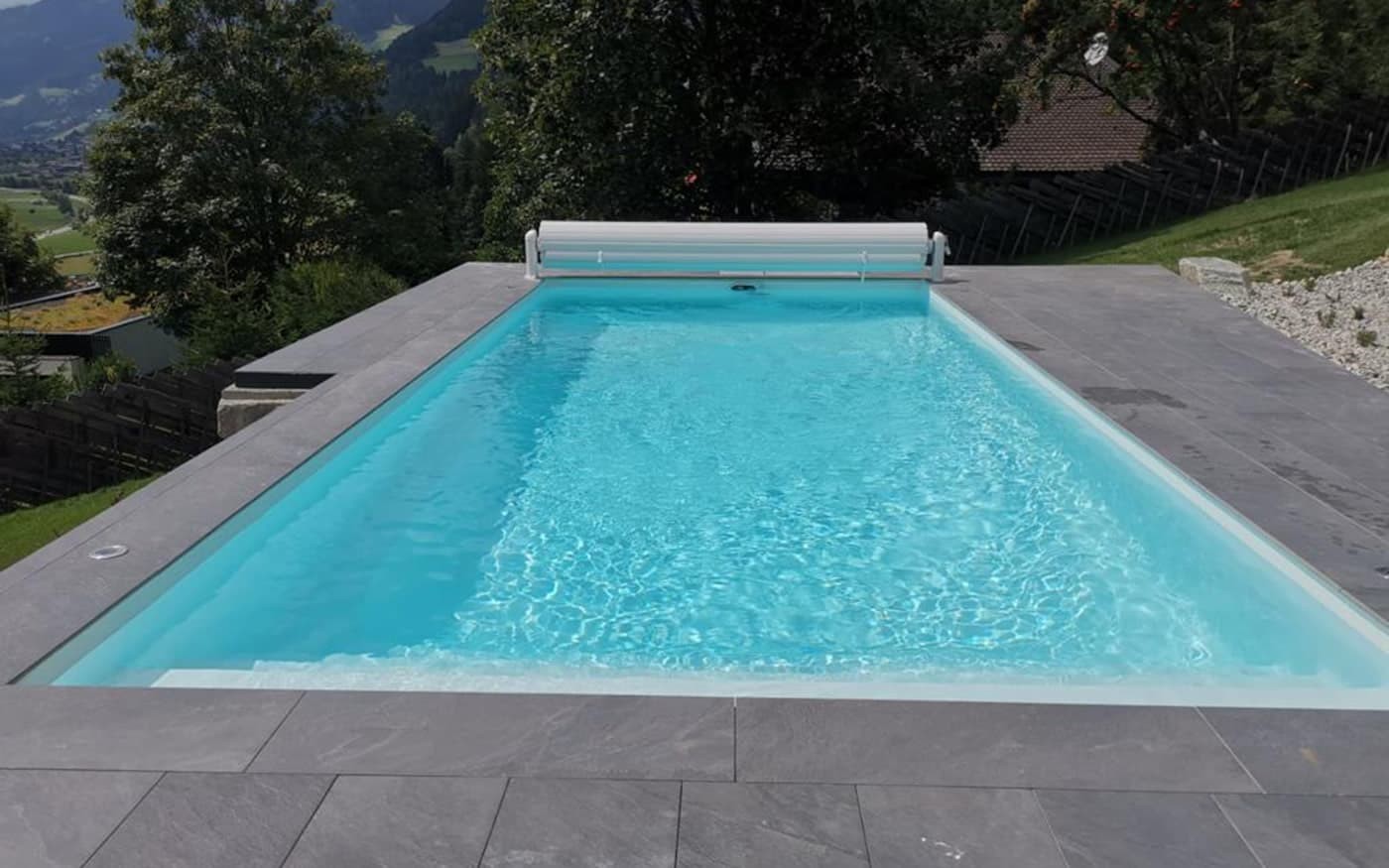 Ein rechteckiger Pool Desjoyaux mit klarem Wasser, umgeben von grauen Fliesen, drau&szlig;en in Landschaft