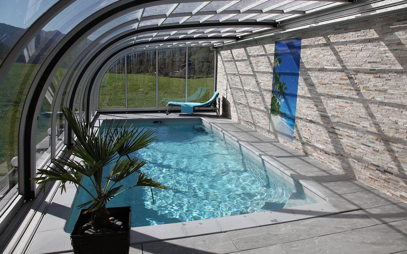 Moderner &uuml;berdachter Pool Desjoyaux mit Liegestuhl und Palme neben einer Ziegelsteinwand