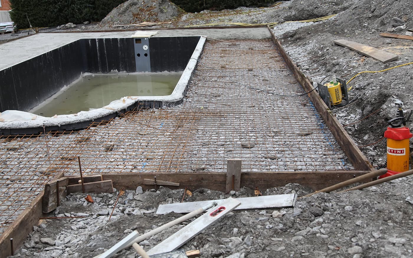 Baustelle mit einem teilweise gef&uuml;llten Schwimmbecken und einem Bereich mit Stahlbewehrung