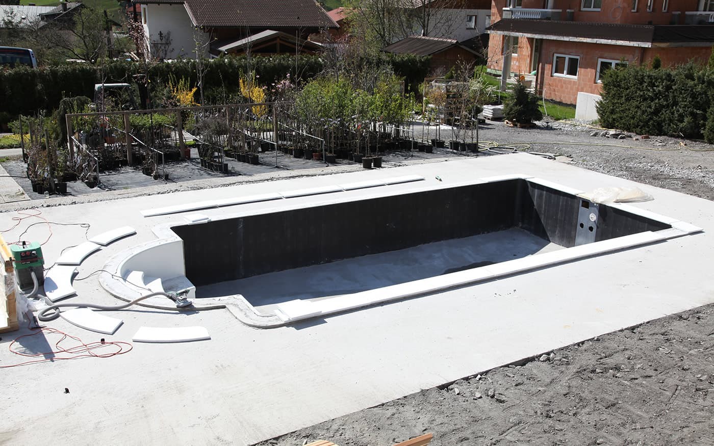Ein rechteckiger Pool im Rohbau auf einer Baustelle mit angrenzenden Pflanzen