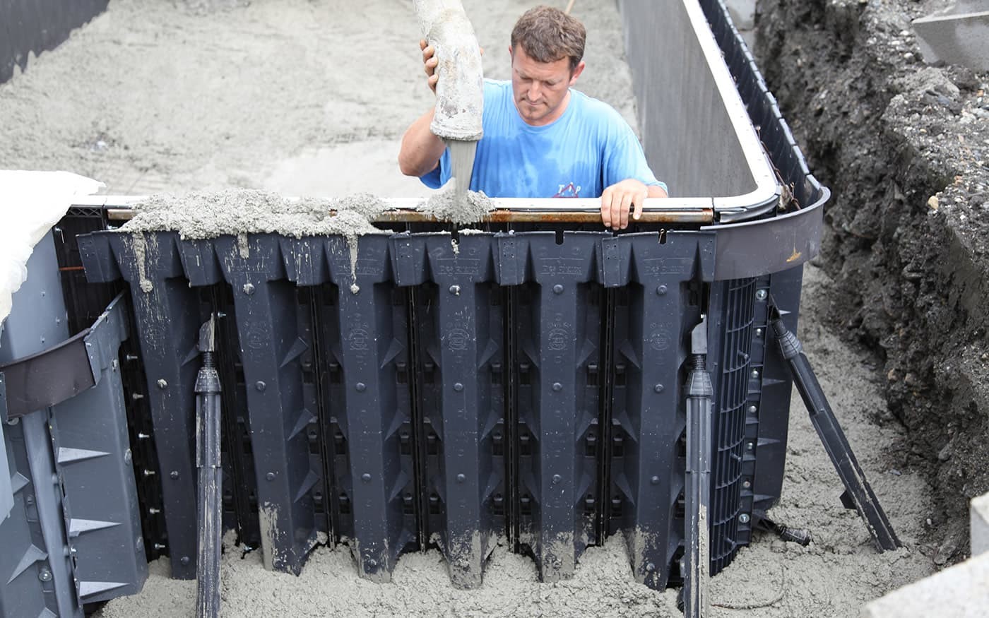 Ein Mann gie&szlig;t Beton in eine Schalung f&uuml;r den Bau eines Pools