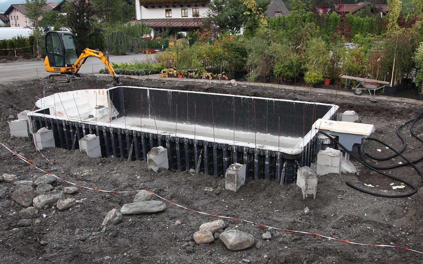 Baustelle f&uuml;r ein rechteckiges Betonbecken mit Bagger im Hintergrund