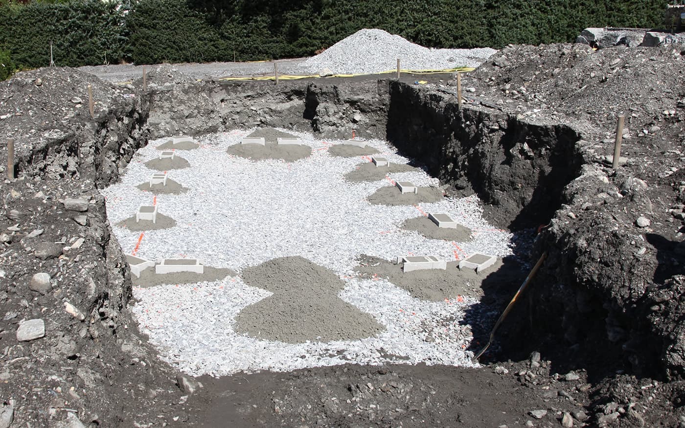 Grube mit Schotterunterbau und gegossenen Betonfundamenten auf einer Baustelle