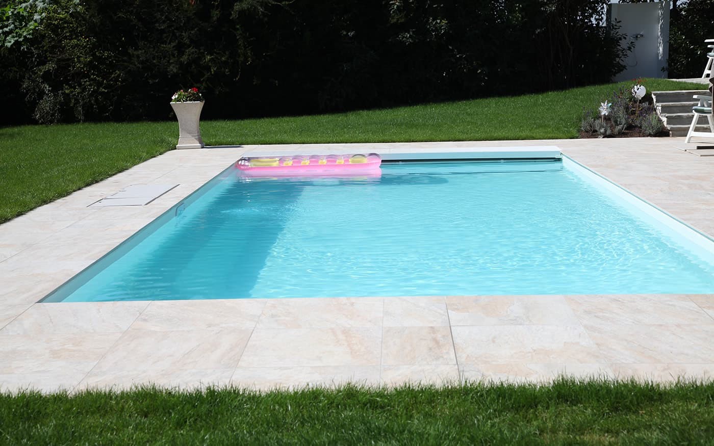 Ein rechteckiger Pool Desjoyaux mit einer rosa Luftmatratze und umgeben von gr&uuml;nem Rasen