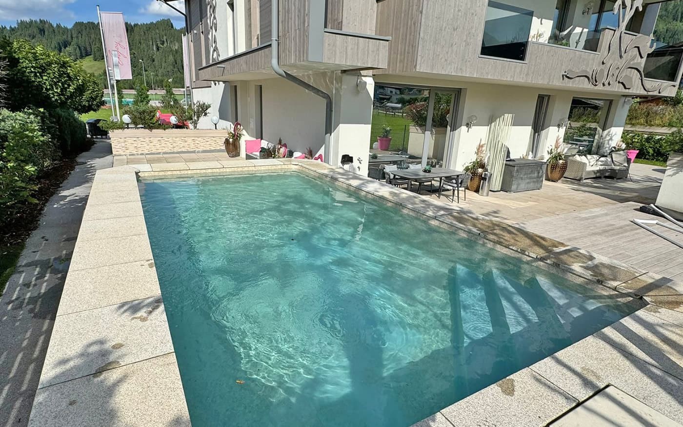 Ein moderner Au&szlig;enpool Desjoyaux neben einem Haus mit Terrasse und Garten im Hintergrund