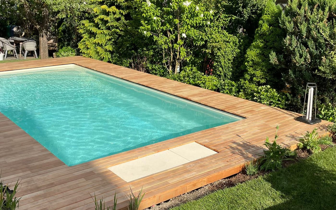 Ein rechteckiger Swimmingpool von Desjoyaux mit Holzumrandung in einem gr&uuml;nen Garten