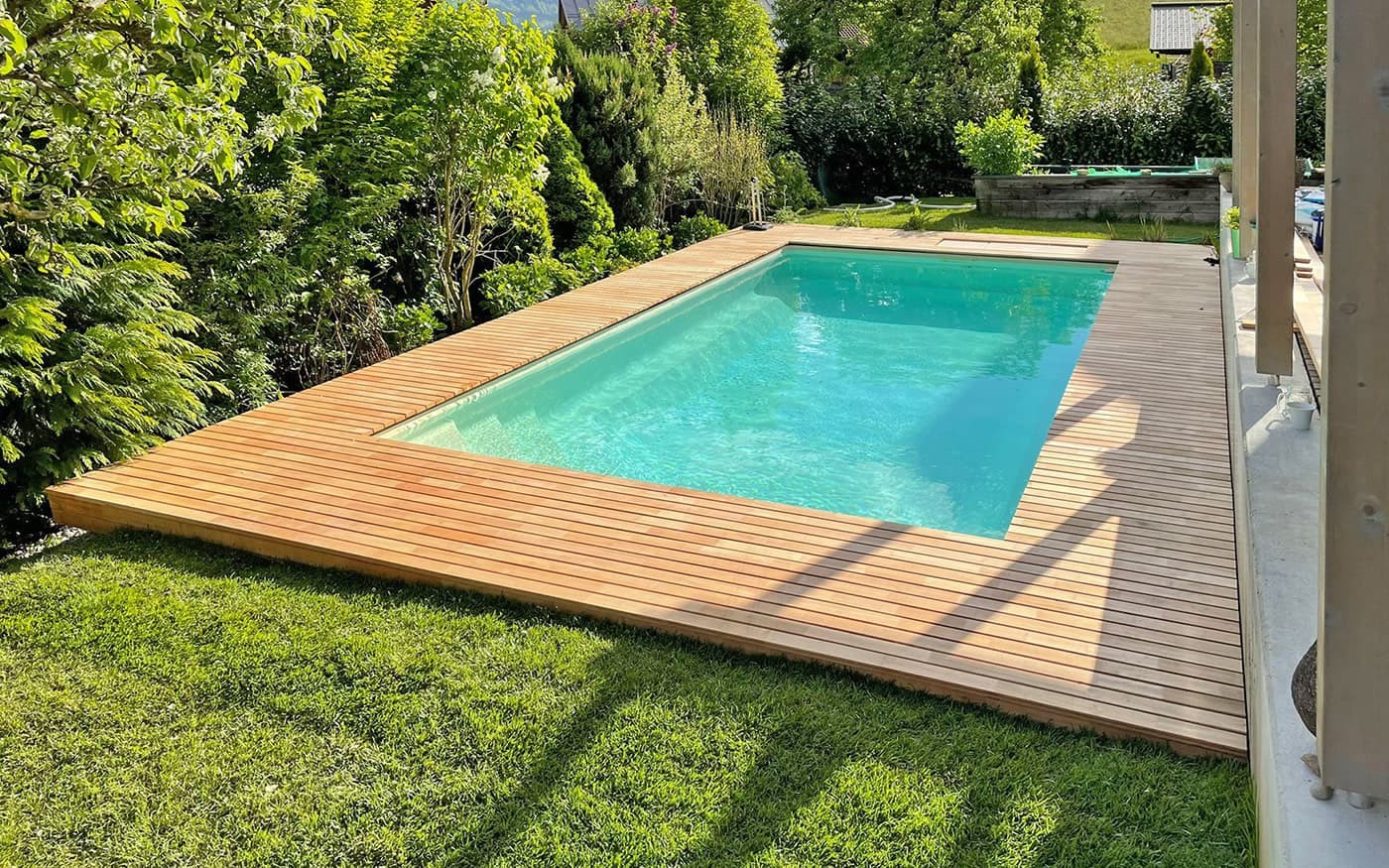 Ein kleiner, rechteckiger Pool Desjoyaux mit Holzumrandung im Garten