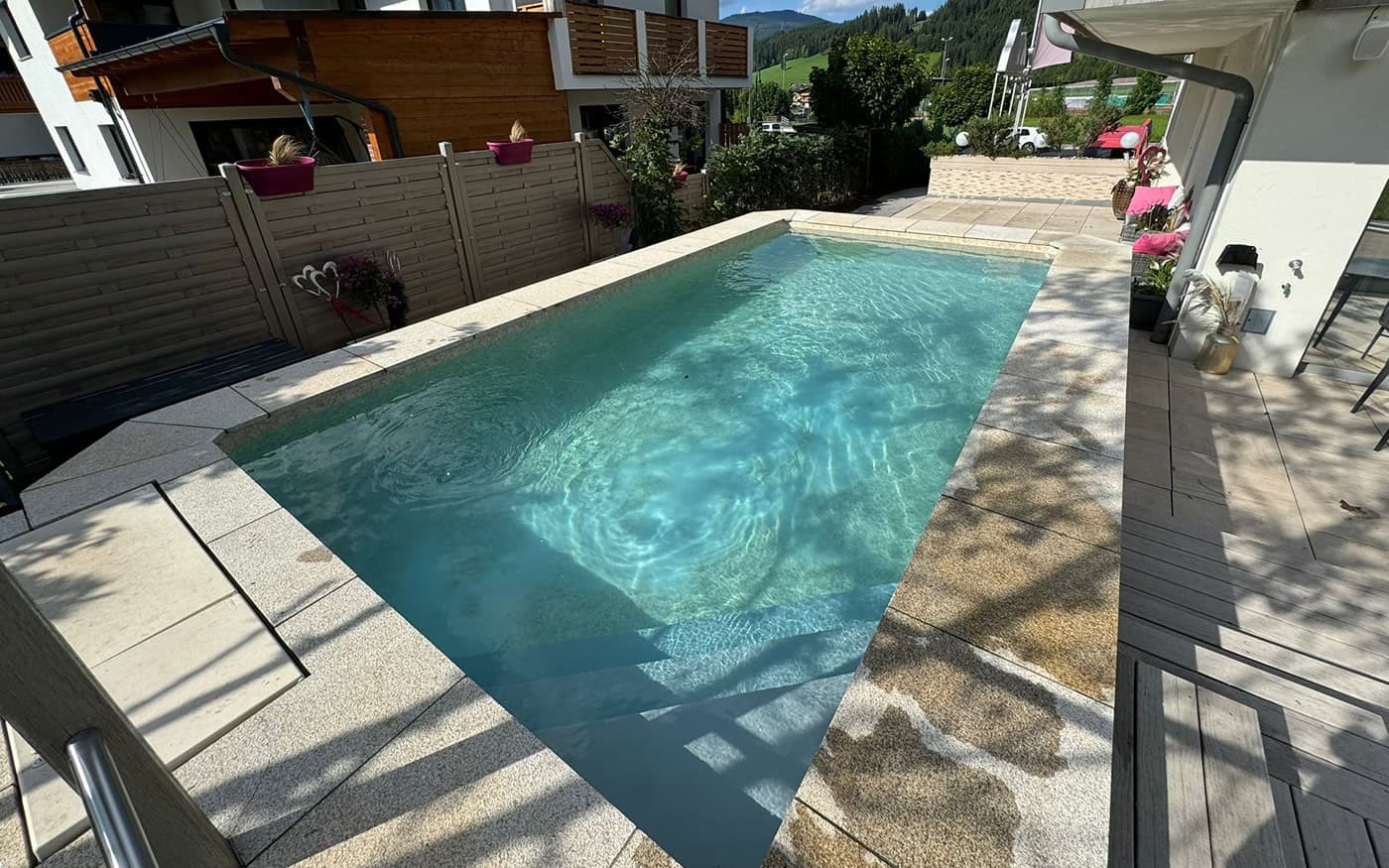 Kleiner Au&szlig;enpool Desjoyaux im Sonnenschein, umgeben von Holzterrasse und bepflanzten T&ouml;pfen