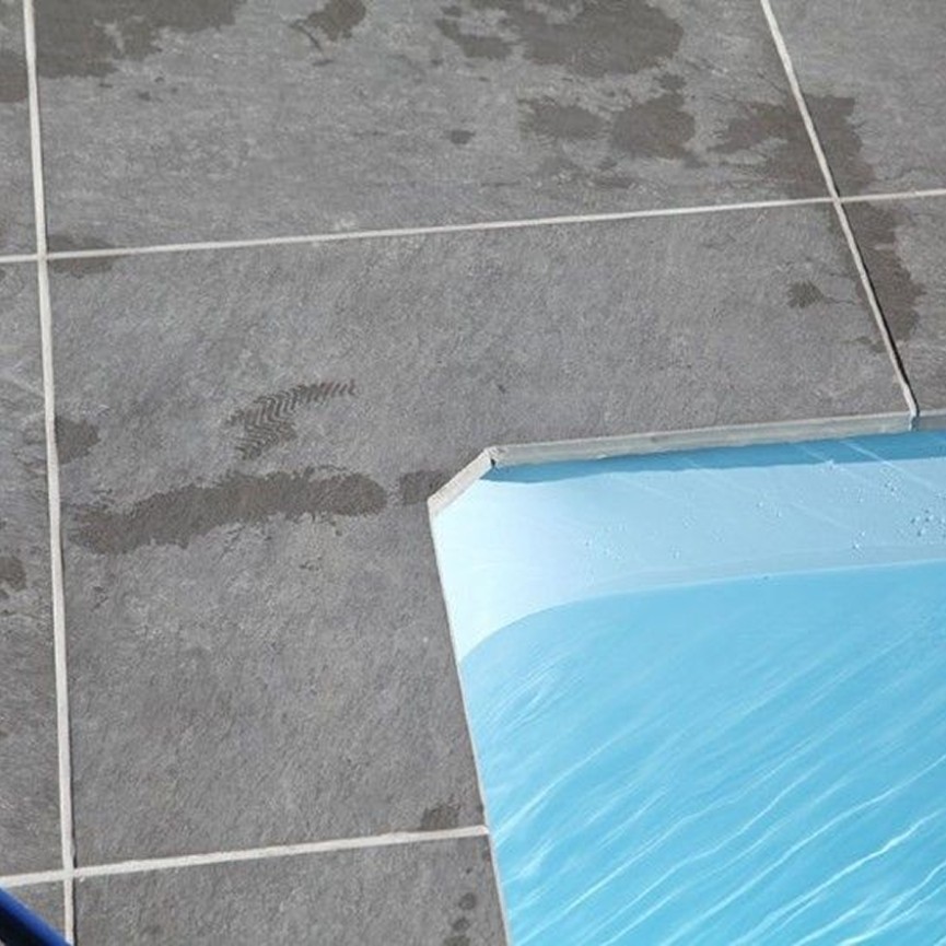 Graue Fliesen grenzen an blaues Wasser eines Pools Desjoyaux, mit nassen Fu&szlig;abdr&uuml;cken darauf