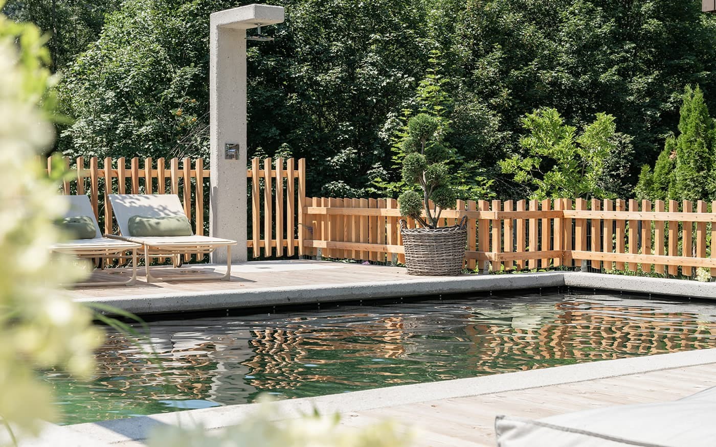 Privater Poolbereich mit Holzterrasse, Liegen und gr&uuml;ner Bepflanzung im Hintergrund