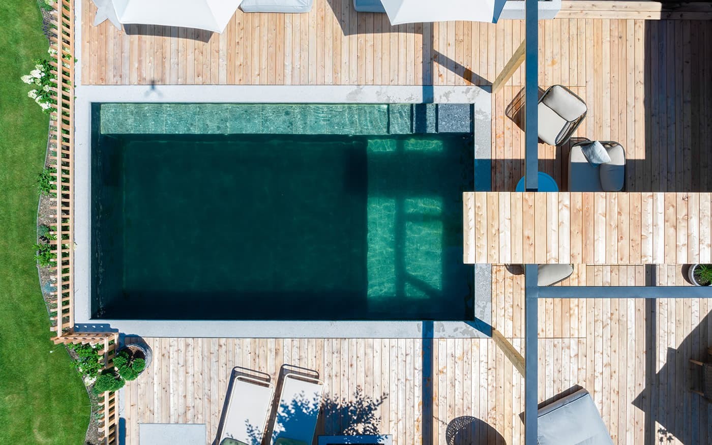 Kompakter Pool auf einer Holzterrasse mit Liegest&uuml;hlen und Sonnenschirmen von oben