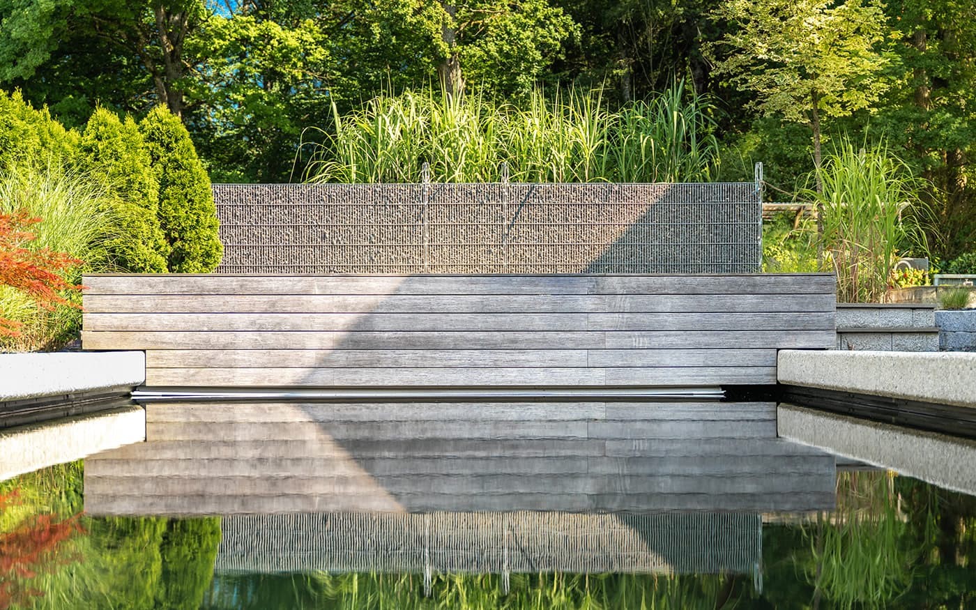 Ein moderner Garten mit Teich und Holzbank, umgeben von &uuml;ppigen Pflanzen und B&auml;umen