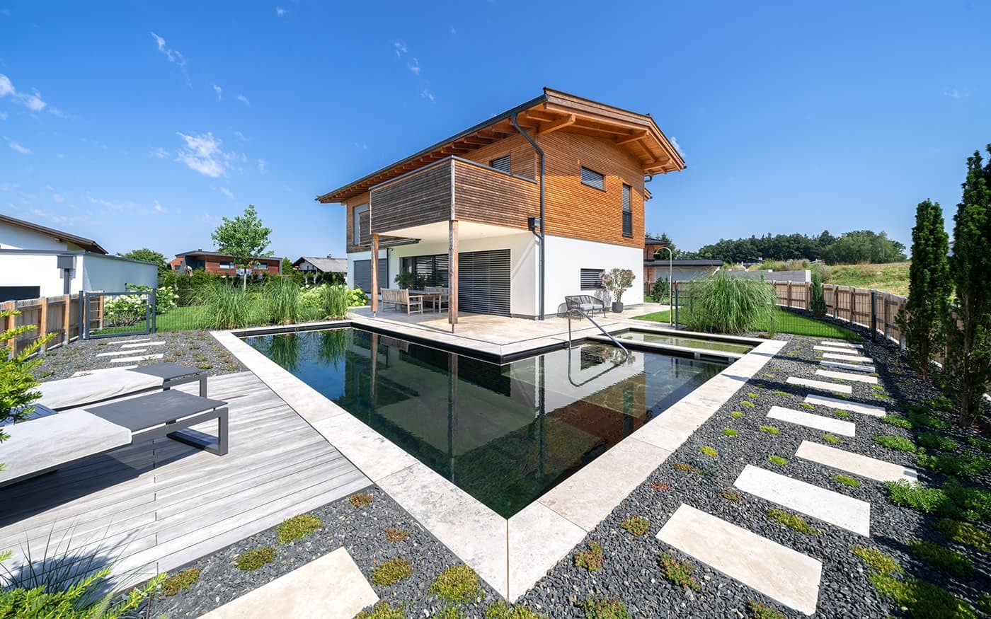 Modernes Haus mit Holzfassade und kleinem Pool im Garten, umgeben von Rasen und Pflanzen