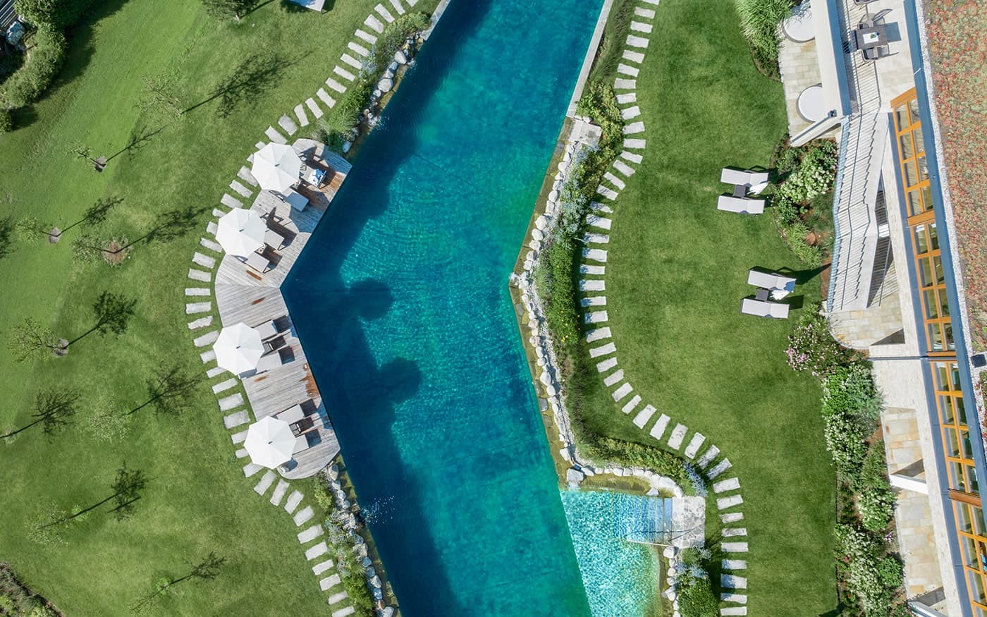 Ein gro&szlig;er, blaugr&uuml;ner Pool ist von gr&uuml;nen Rasenfl&auml;chen und Liegest&uuml;hlen umgeben