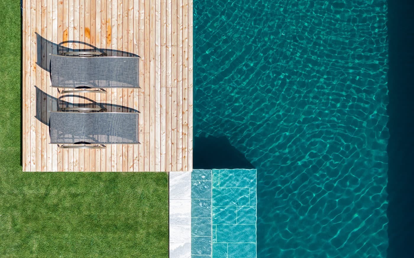 Zwei Liegest&uuml;hle auf einer Holzplattform neben einem blauen Pool