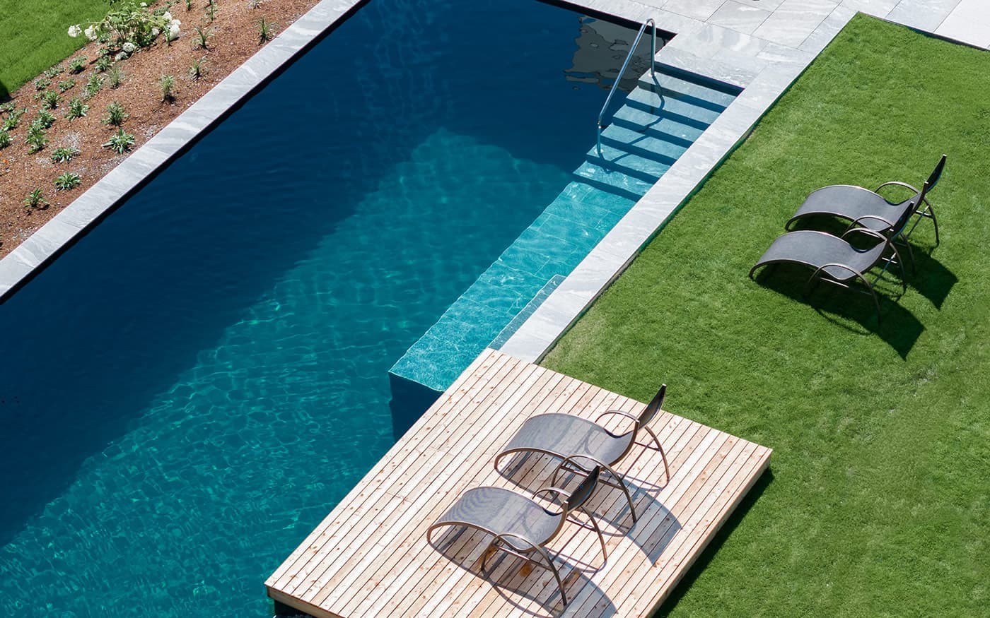 Moderner Pool mit Holzterrasse und Liegest&uuml;hlen auf gr&uuml;nem Rasen
