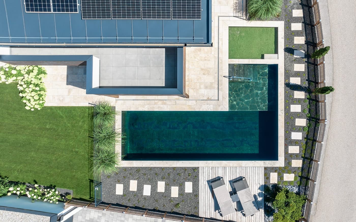 Luftaufnahme eines modernen Gartens mit Pool, Liegest&uuml;hlen und Solarpanelen auf dem Dach