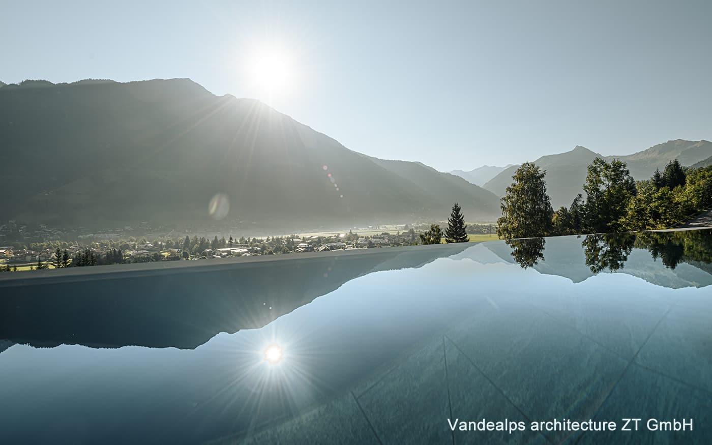 Ein Infinity-Pool spiegelt Berge und B&auml;ume im Morgenlicht wider