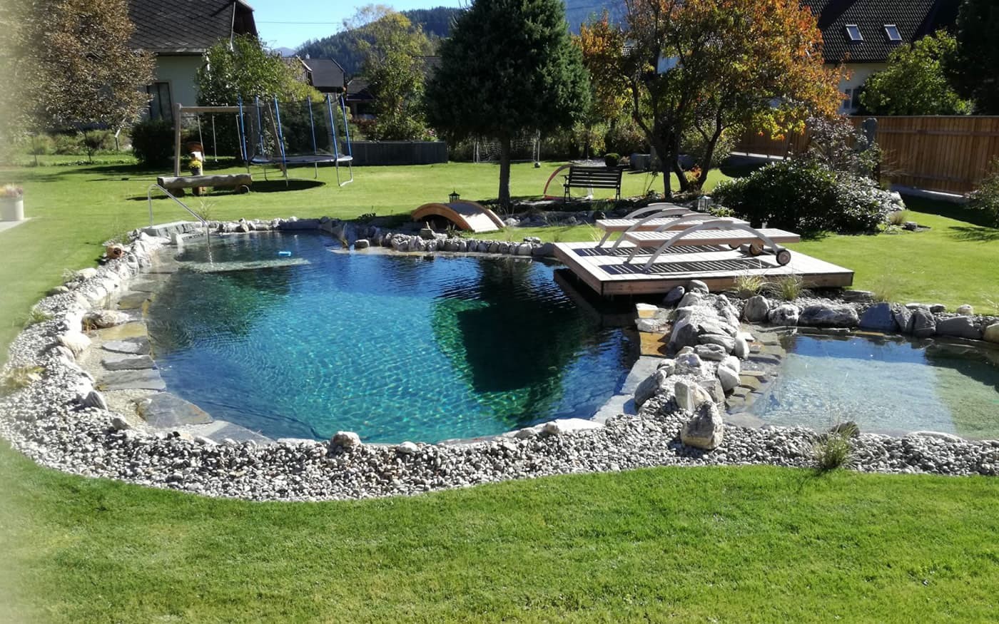 Ein nat&uuml;rlicher Schwimmteich im Garten mit Liegest&uuml;hlen auf einem Holzdeck