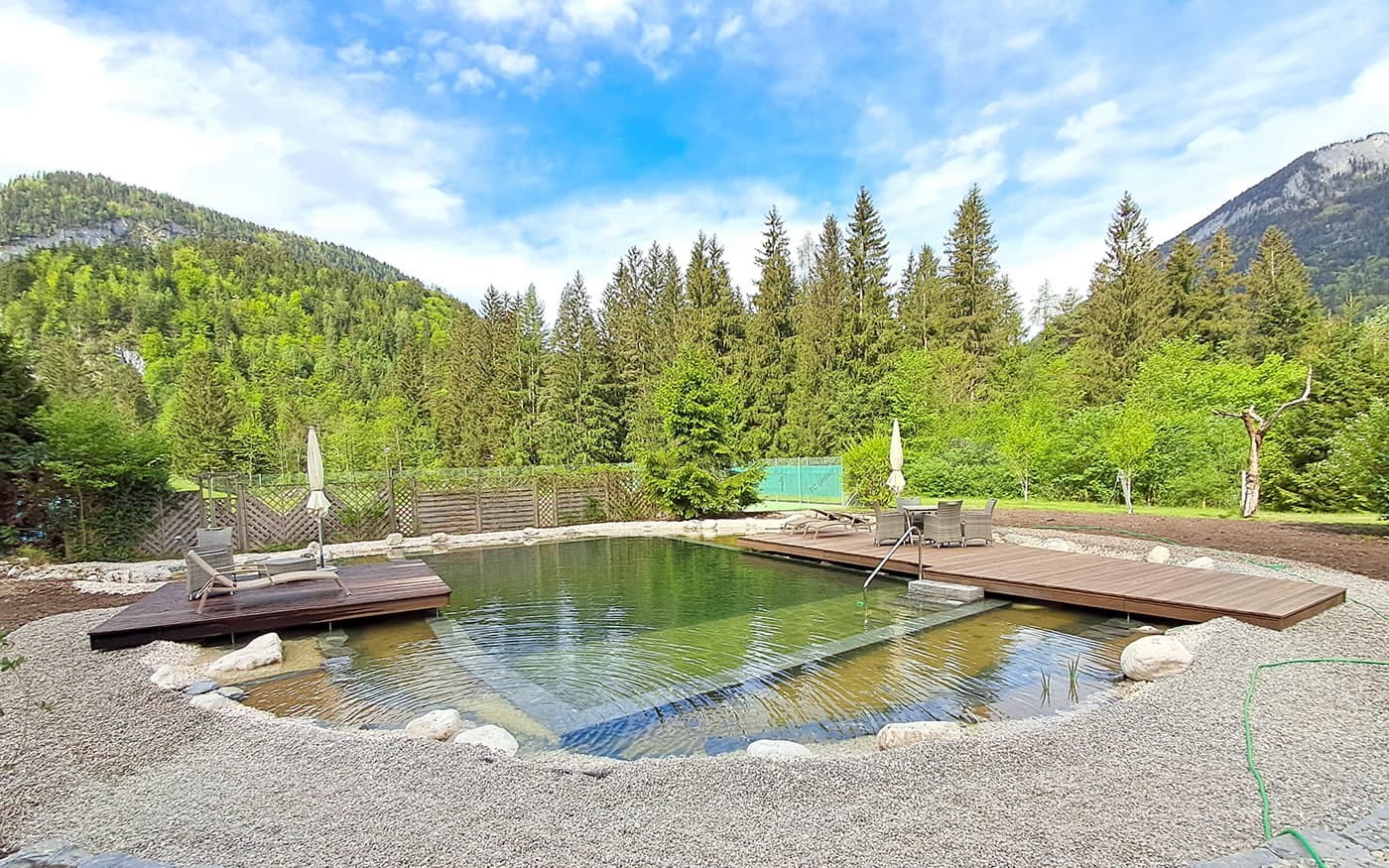 Ein nat&uuml;rlicher Teich mit Holzstegen liegt inmitten einer Waldlandschaft mit Bergen